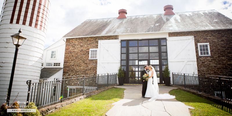 A newlywed couple standing in front of a barn and silo kissing