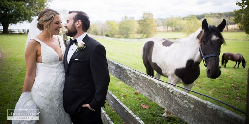 A newlywed couple staring into each others' eyes standing next to a horse
