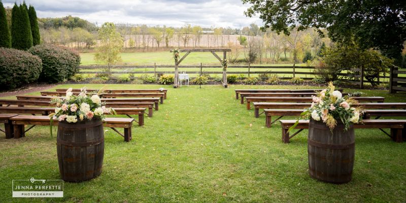 A detail shot of the wedding venue, showing wooden benches on top of well-kept grass. A wooden wedding arch sits in the distance of the picture, looking out onto a field.