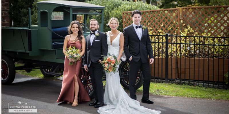 A newlywed couple posing with friends in front of a vintage car