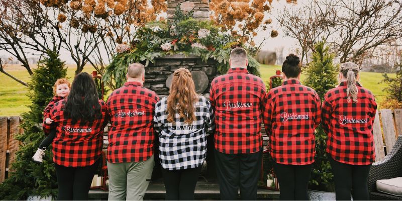 A group of people standing with their backs to the camera wearing flannels that read "bridesmaid, brides man, and bride".