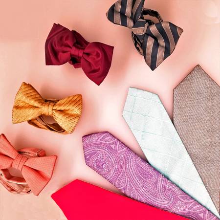 A variety of bow ties and neckties in different colors and patterns are arranged on a peach-colored surface. The collection includes striped, paisley, solid, and textured designs.